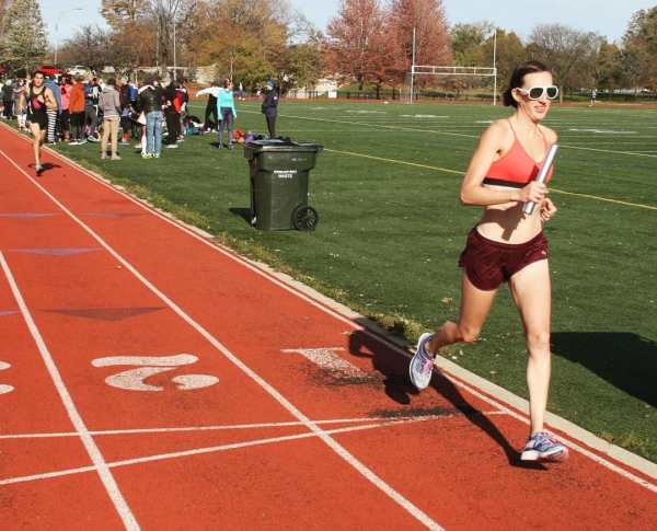 Author running a mile relay on the track in a sports bra and shorts.